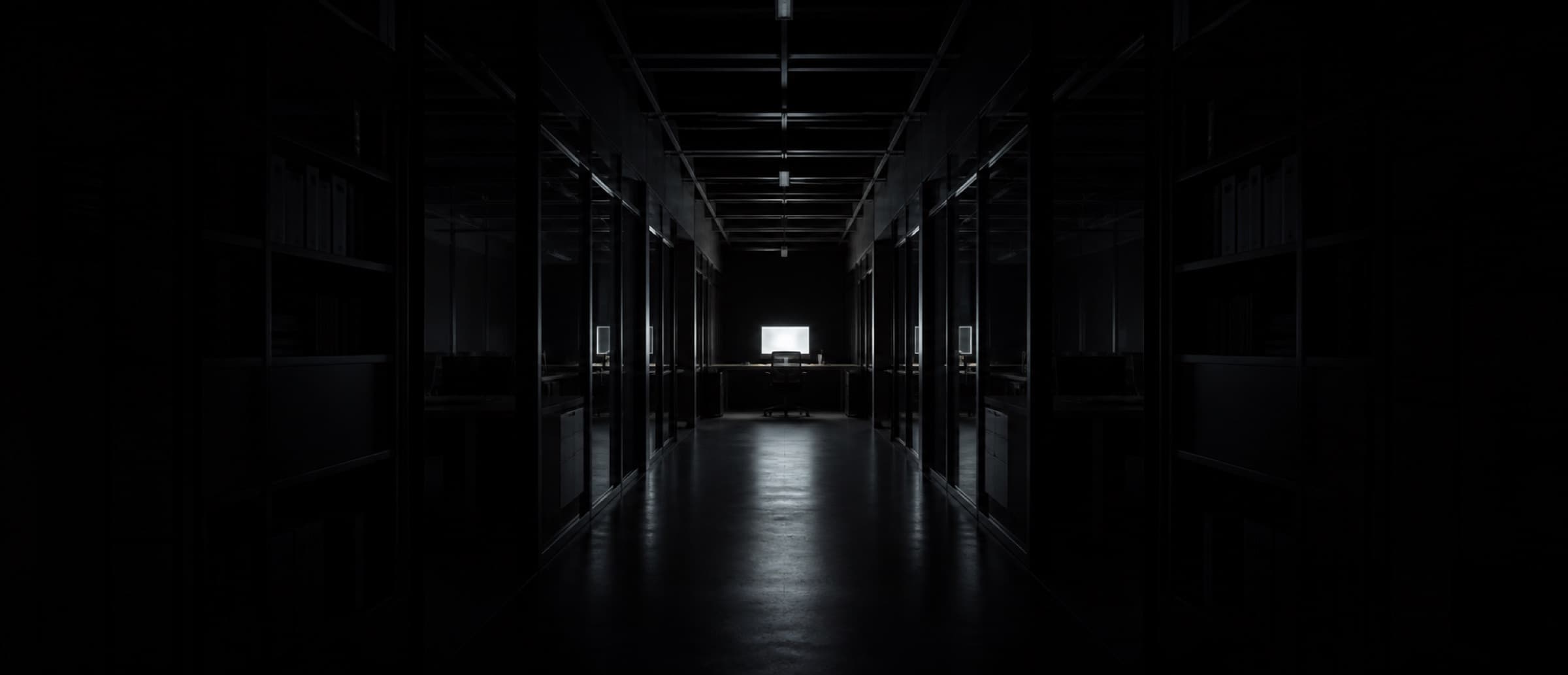 A dark office corridor at night, a single monitor glowing at the far end