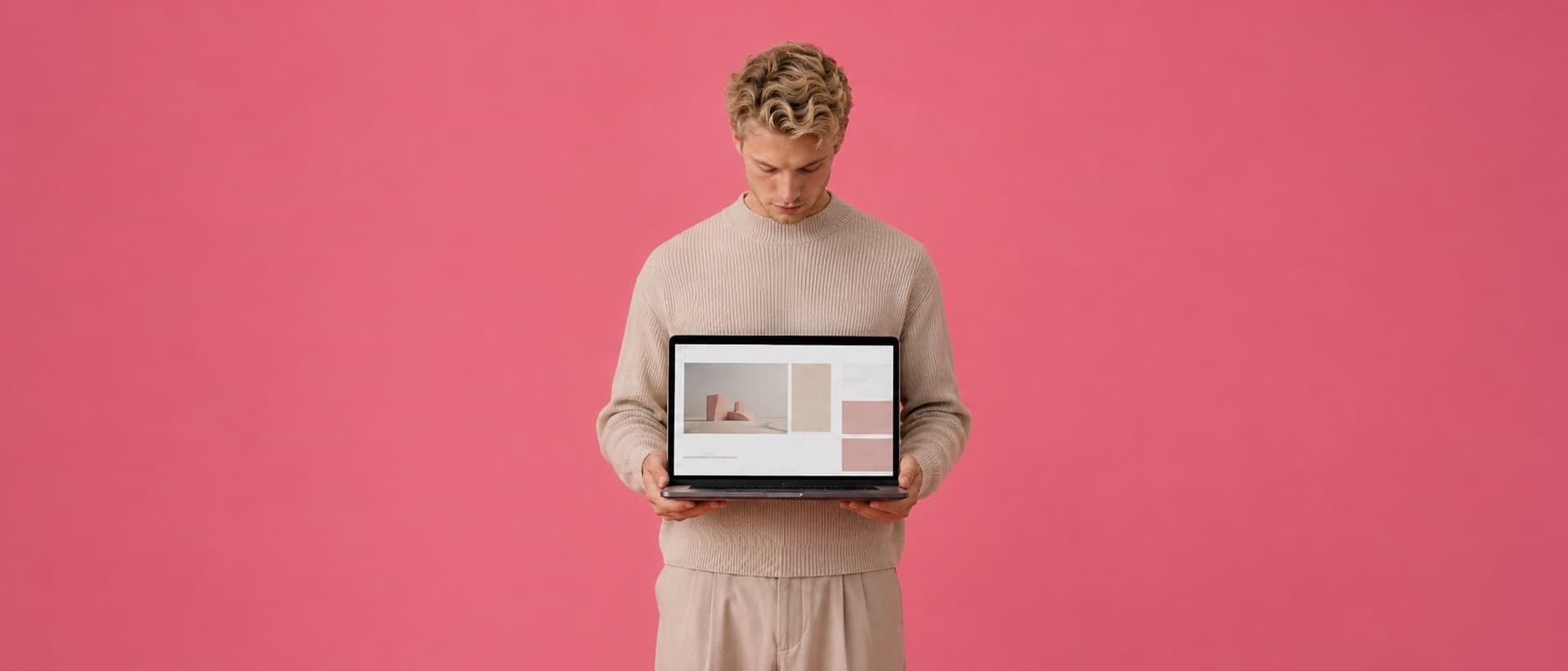 An agency founder against a pink backdrop holding a laptop that shows a finished website